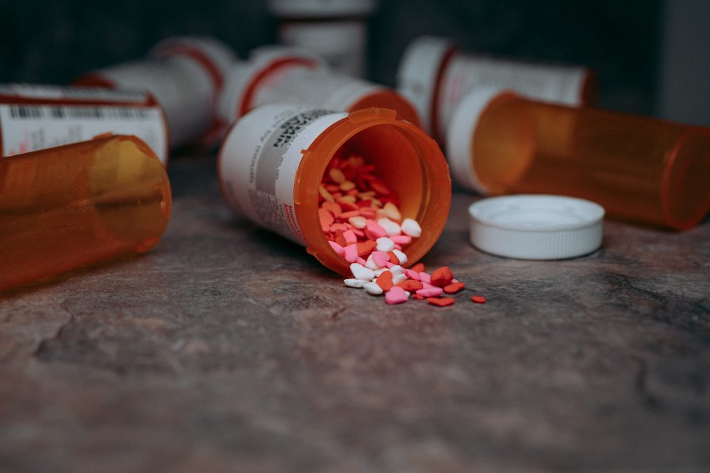 Eine Pillendose, die umgekippt ist und aus der unzählige Pillen in unterschiedlichen Formen ausgeschüttet wurden.